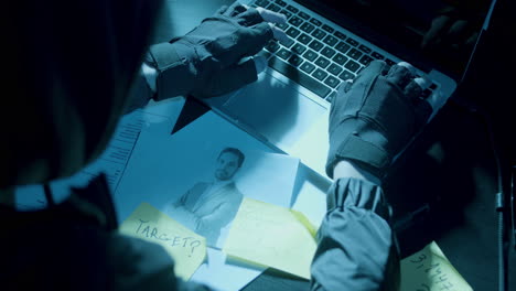 unrecognizable man in hood wearing fingerless gloves and typing on keyboard