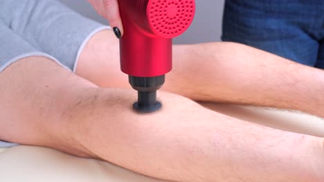 masajista femenina masajeando los músculos de la pantorrilla de un deportista con un masajeador de percusión