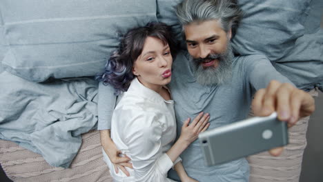 una pareja tomando una selfie en la cama.