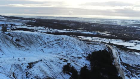 Schneebedeckter-Rivington-Pike-Tower-Winterhügel-Antenne-Langsame-Schwenkung-Rechte-Ansicht-Leute,-Die-Bei-Sonnenaufgang-Bergab-Rodeln