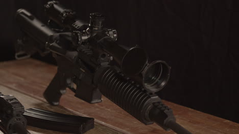 close dolly of ar 15 rifle with scope standing on wooden table