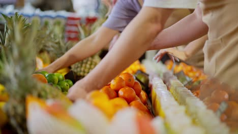 Close-up-a-guy-and-a-girl-supermarket-workers-sort-fruits-and-pineapples-orange-fruits-on-a-shelf-in-a-supermarket