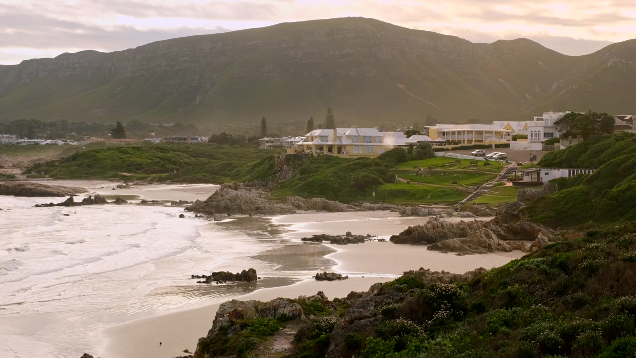 Spiaggia di Voëlklip a Hermanus illuminata dalla calda luce del tramonto, vista dall'alto.