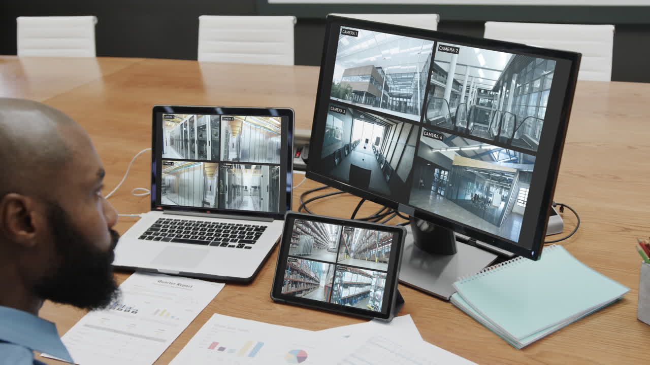 African american male security officer watching cctv camera views on computer screens, slow motion