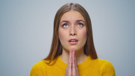 portrait of attractive young woman praying at camera on grey background.