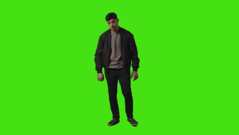 toma completa de un joven vestido casualmente de pie y esperando contra la pantalla verde