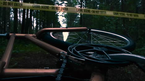low angle slow motion footage of a bronze and golden colored bicycle fallen over on a dirt muddy dark forest road with a yellow crime scene tape hanging above it idicating foul play or investigation