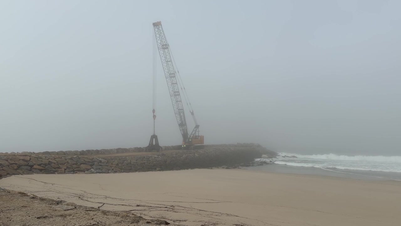 Scatto suggestivo di una gru industriale che solleva un enorme masso frangiflutti per la difesa costiera a Furadouro, Portogallo.