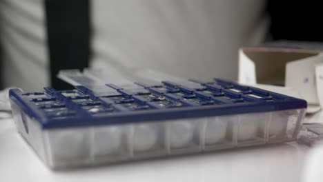 old man sorting medicine pills by weekly organizer box - extreme close up