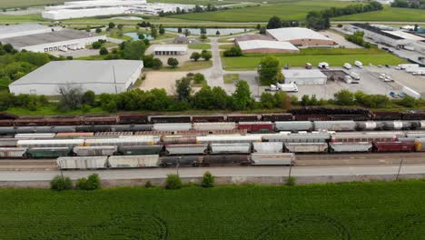 Imágenes-Aéreas-De-4k-Que-Se-Desplazan-De-Izquierda-A-Derecha-De-Varios-Trenes-Y-Vías-Con-Un-Tren-Comenzando-A-Moverse-Y-Un-Pequeño-Pueblo-En-El-Fondo