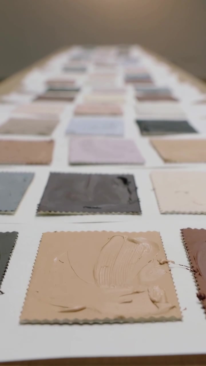Vertikales Video: Von rechts kommende, schwarz behandschuhte Hand verschmiert eine beige Farbprobe auf einem Studiotisch, testet Farbe