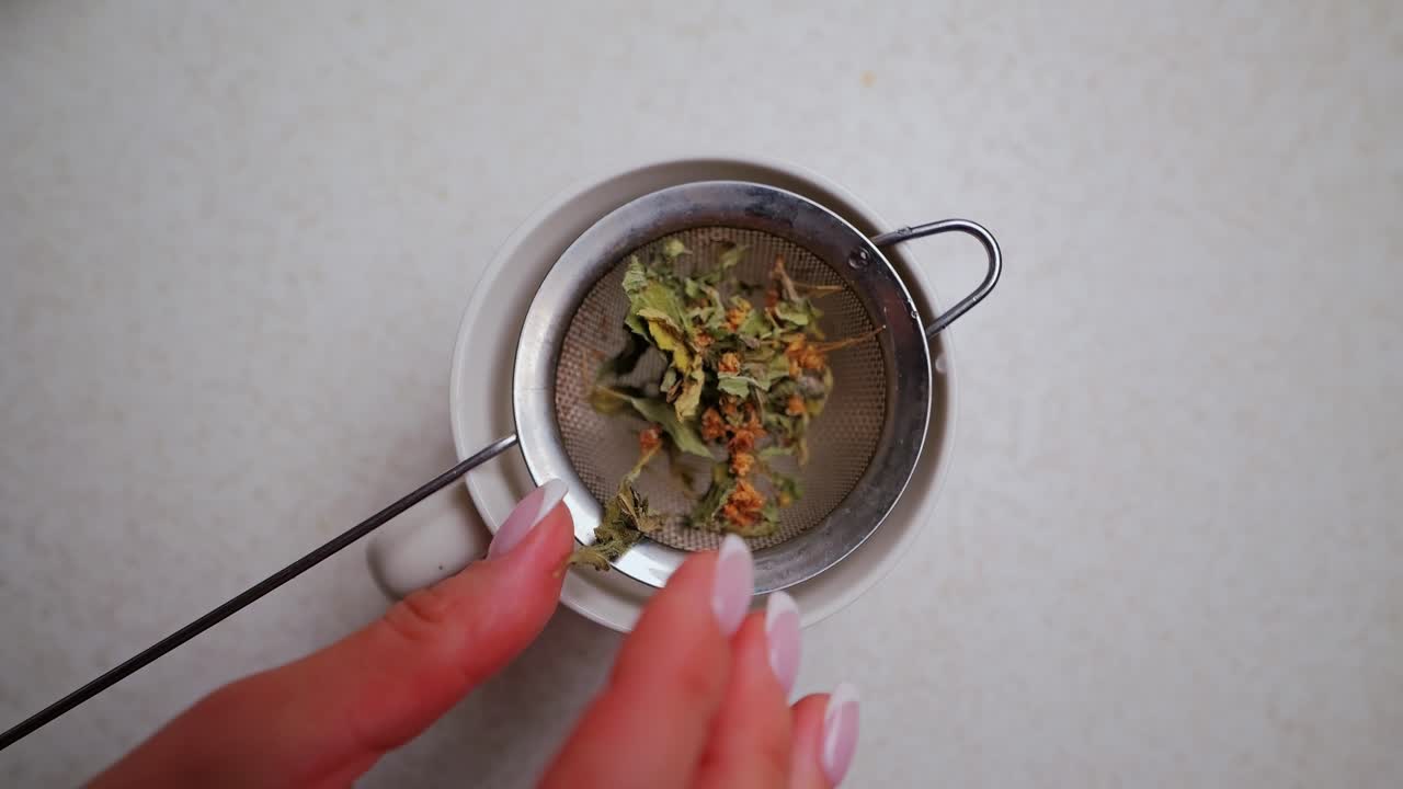 Close-up of hands adding aromatic dried herbs into tea strainer slowly