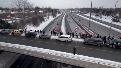 Sobrevuelo-Cinematográfico-De-Manifestantes-Canadienses-Ondeando-Banderas-De-Pie-En-El-Puente-De-La-Carretera-En-Apoyo-De-La-Libertad-Mientras-Los-Camiones-Pasan