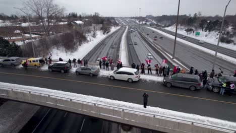 sobrevuelo cinematográfico de manifestantes canadienses ondeando banderas de pie en el puente de la carretera en apoyo de la libertad mientras los camiones pasan