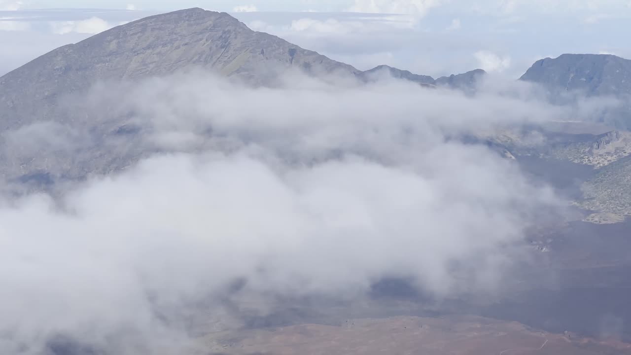 Cinematic close-up panning shot of thick clouds blanketing the volcanic crater at the summit of Haleakala in Maui, Hawai'i