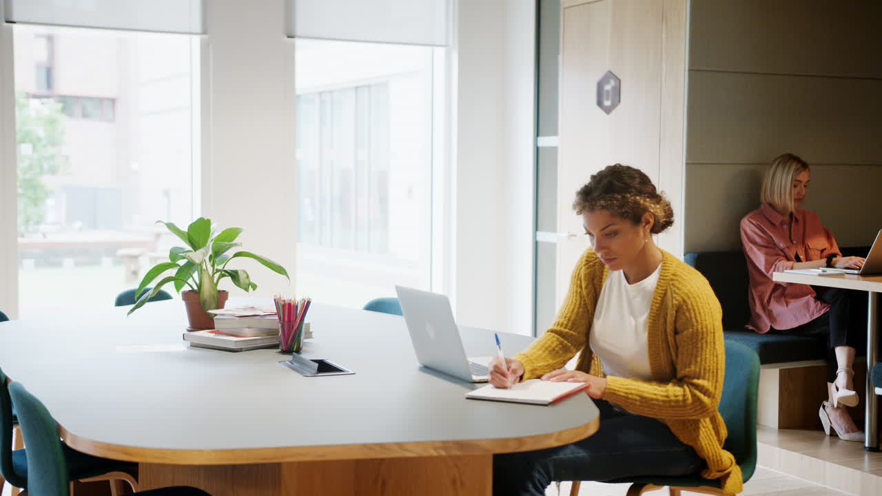 Two millennial women working at laptop computers sitting in a creative office, close up