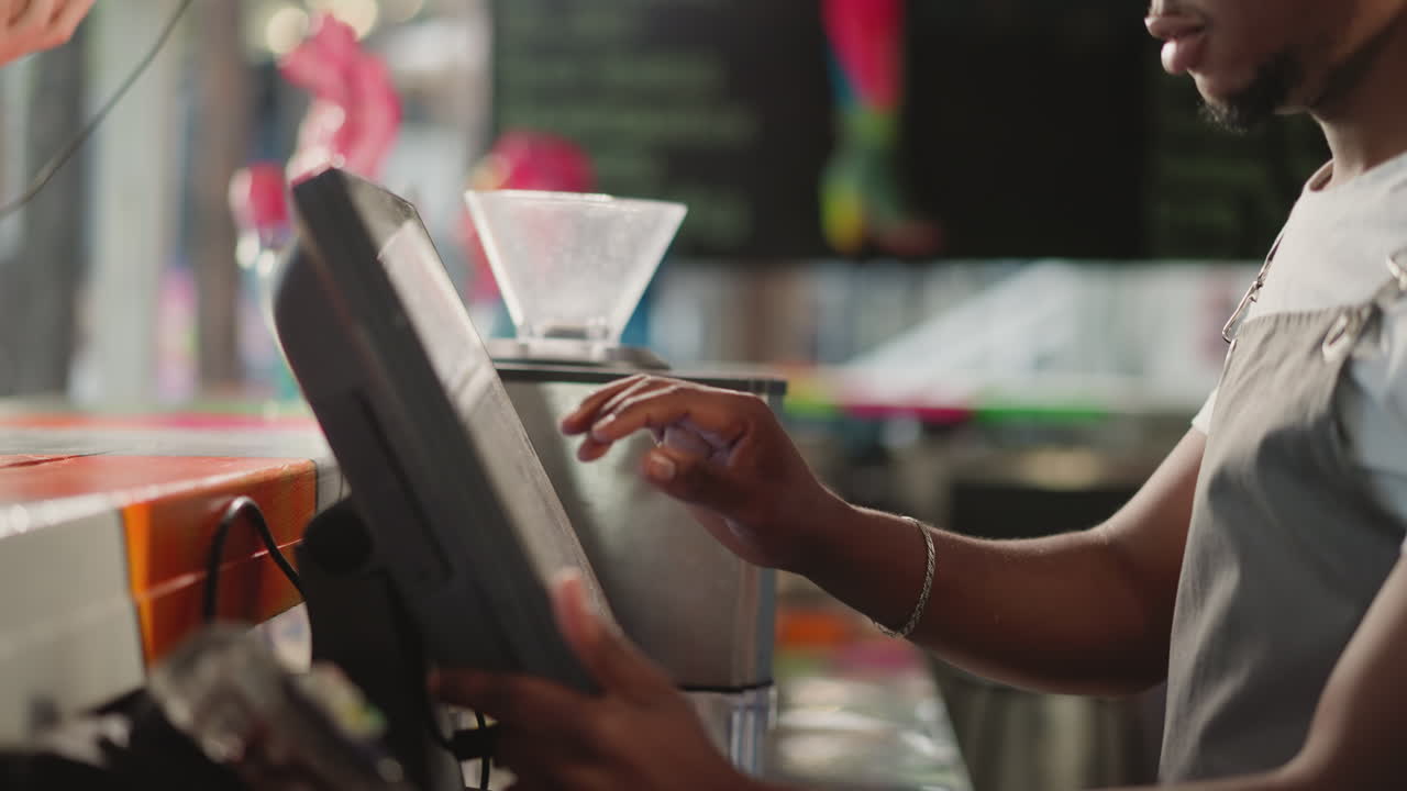 Shop assistant works on computer at counter closeup. African American employee inputs order data in base at counter. Cashier prepares bill at desk