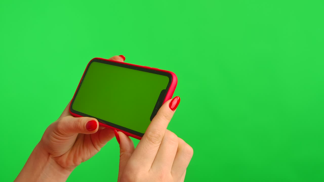 Female hand holds mobile phone with workspace mock up screen on green background in horizontal position. Woman touches screen, clicks and browses content on Internet. Advertising area. Close up