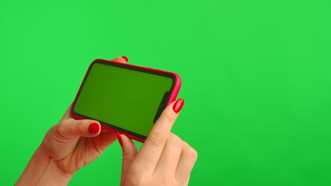female hand holds mobile phone with workspace mock up screen on green background in horizontal position. woman touches screen, clicks and browses content on internet. advertising area. close up