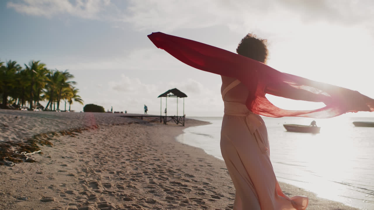 Woman with flowing red scarf on a tropical beach at sunset
