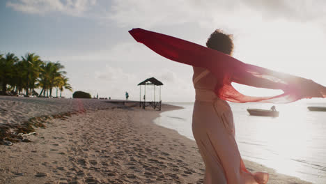 woman with flowing red scarf on a tropical beach at sunset