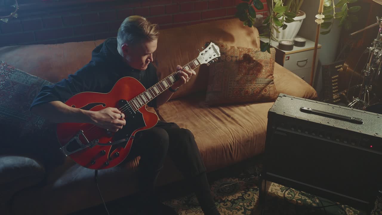 Man playing jazz guitar on a couch in a home studio
