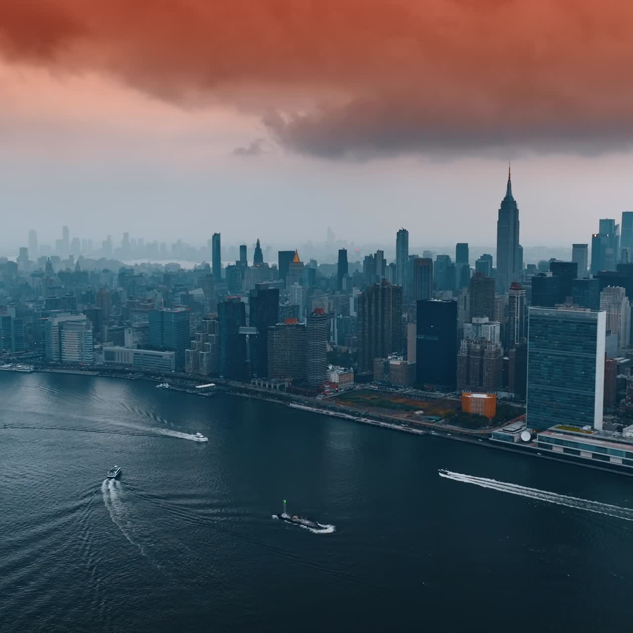 Boat and yachts float by the Hudson River. New York skyline under the pink cloudscape. Top view