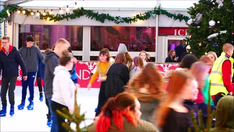 winchester christmas market people ice skating around a large christmas tree, winchester university logo. christmas ice rink activity, fun skating