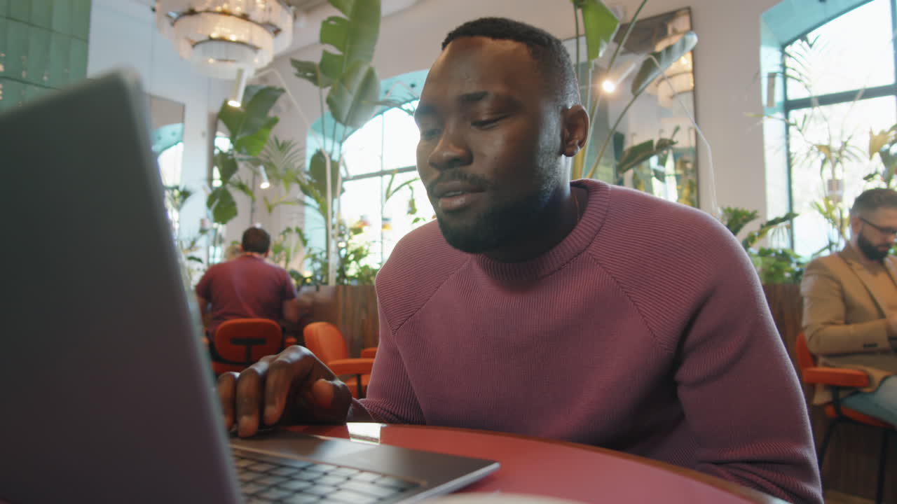 African American Man Chatting via Video Call on Laptop in Cafe