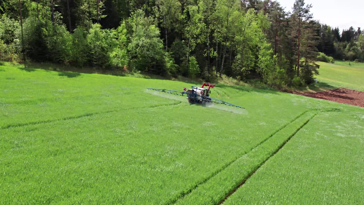 Zoom out shot of red tractor spraying chemicals in a large green field