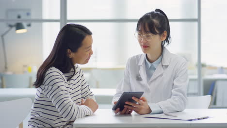 asian female doctor and woman using tablet and talking