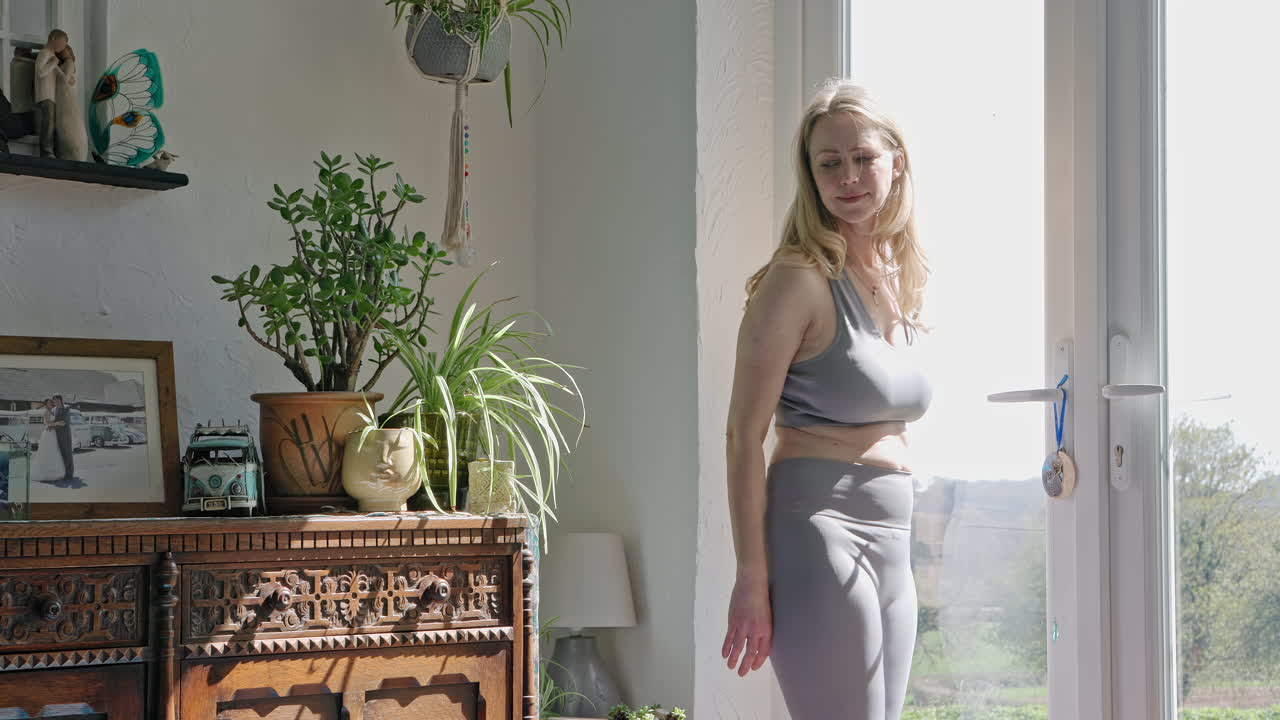 Woman in yoga clothes standing near window in a living room