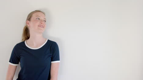 happy caucasian woman in navy blue t shirt with white edging, on white wall, copy space, slow motion