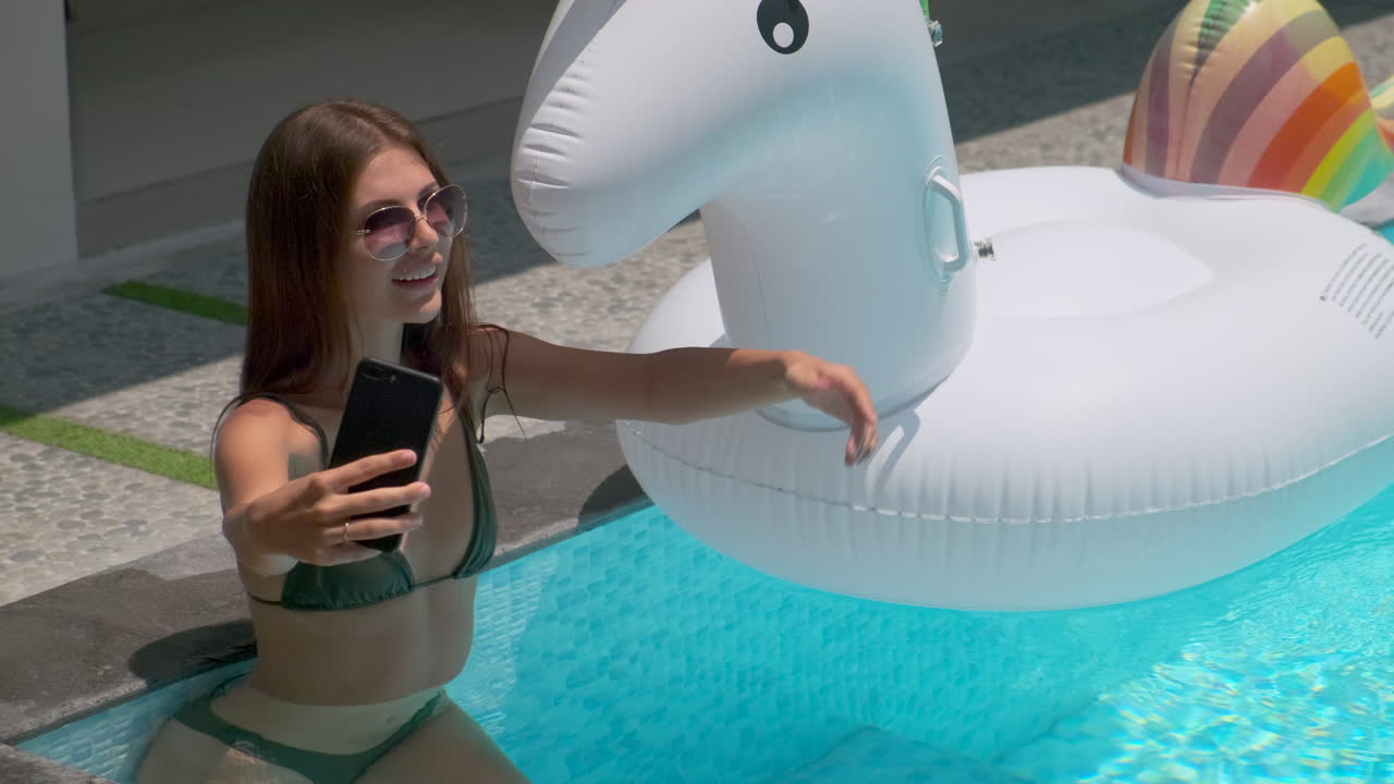 mujer tomando una selfie junto a la piscina con un unicornio inflable