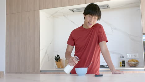 teenage asian boy pours milk into a bowl of cereal at home, with copy space