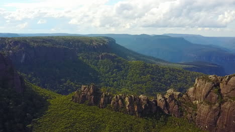 Drone-turning-in-an-arc-revealing-large-rock-structure-and-cliffs-with-mountains-in-the-background