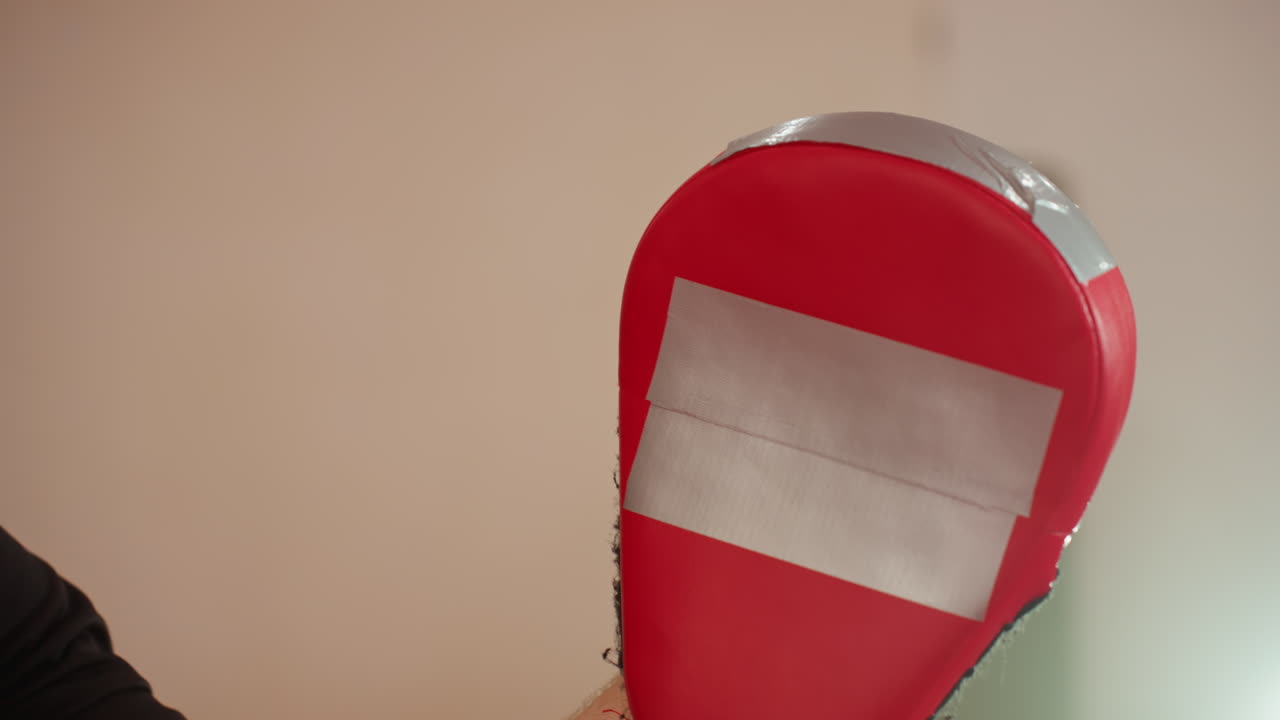 Closeup of red boxing pad with white tape held by trainer during boxer workout in gym, showing wear, detail, and equipment used for combat sports training, athletic preparation
