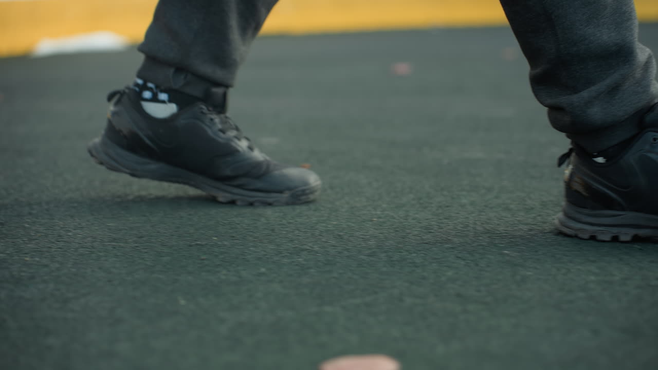 Side leg view of person walking into sports arena, featuring detailed shot of athletic footwear on yellow boundary, urban setting in background