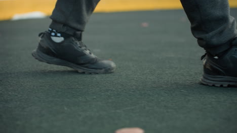 side leg view of person walking into sports arena, featuring detailed shot of athletic footwear on yellow boundary, urban setting in background