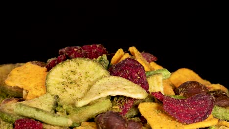 a hand reaches into a colorful pile of assorted dried vegetable chips, picking up pieces under bright, even lighting with a static close-up camera angle