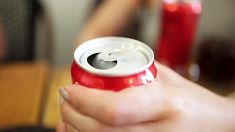 a close-up sequence shows a person’s hand opening a red soda can on a wooden table, with soft natural lighting and shallow depth of field