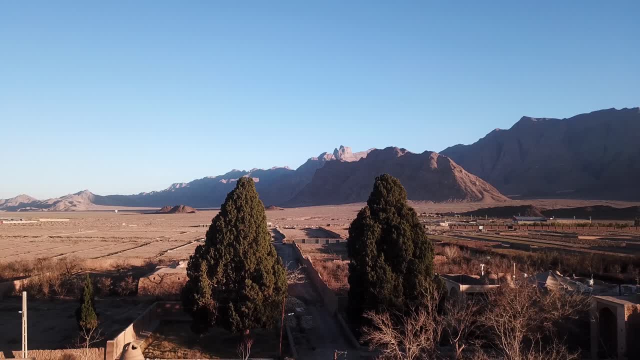 cipreses sagrados gemelos en un pequeño pueblo en irán taft yazd pueblo zoroastriano asentamiento mobarakeh cerca de la carretera y las montañas en el fondo al atardecer en la tarde en la zona desértica