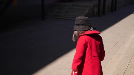 fashionable korean baby girl in a red coat walks down the street in spring