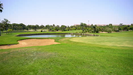 Ein-Wunderschöner-Golfplatz-Mit-Grünem-Gras,-Bäumen,-See-Und-Federgras-An-Einem-Sonnigen-Tag