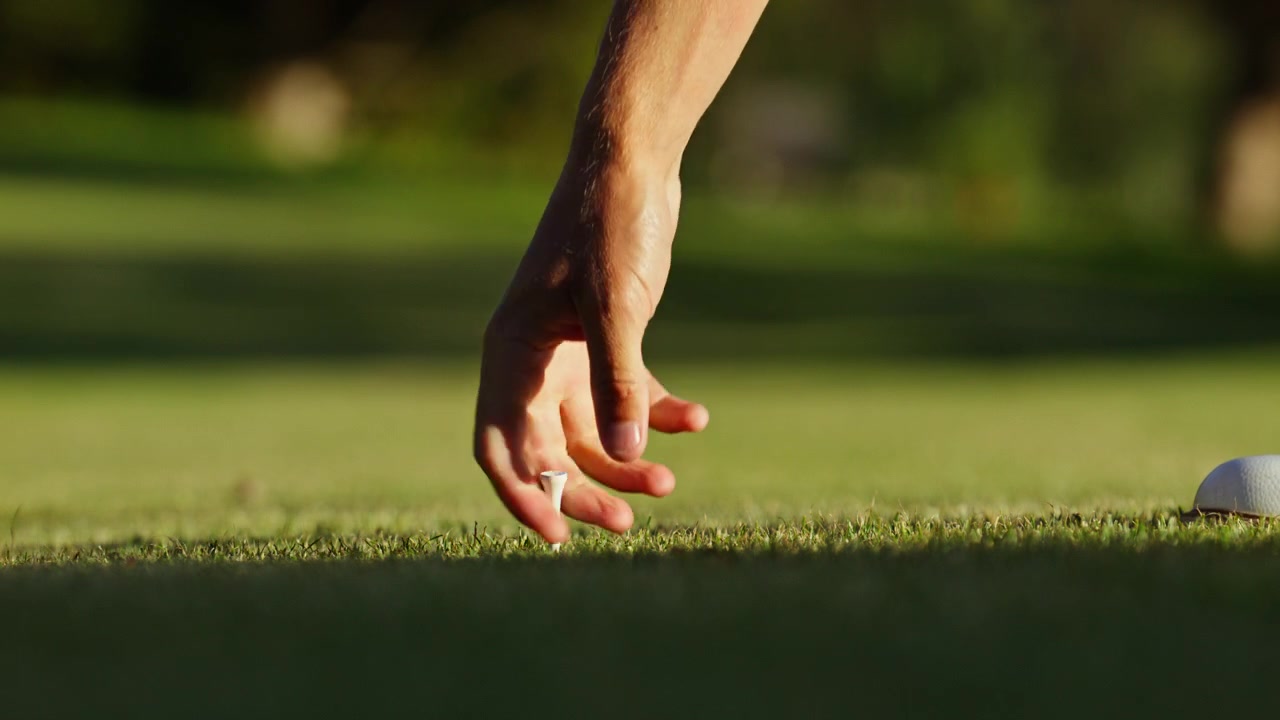 Primo piano cinematografico di un golfista che raccoglie un tee dopo un colpo di partenza su un campo da golf di montagna a Verbier, Svizzera. Momento dettagliato di stile di vita sportivo catturato nella calda luce della sera