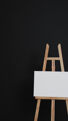 vertical video of white canvas sign with copy space on wooden easel and black background