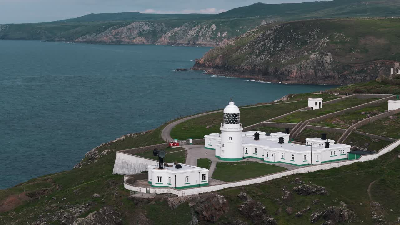 Circle left aerial around Pendeen Lighthouse on Cornwall coast with ocean in background, establishing backdrop