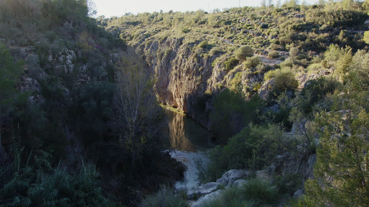 Bright sunlight streaming across winding river flowing between rocky canyon walls, lush greenery framing scenic wilderness landscape