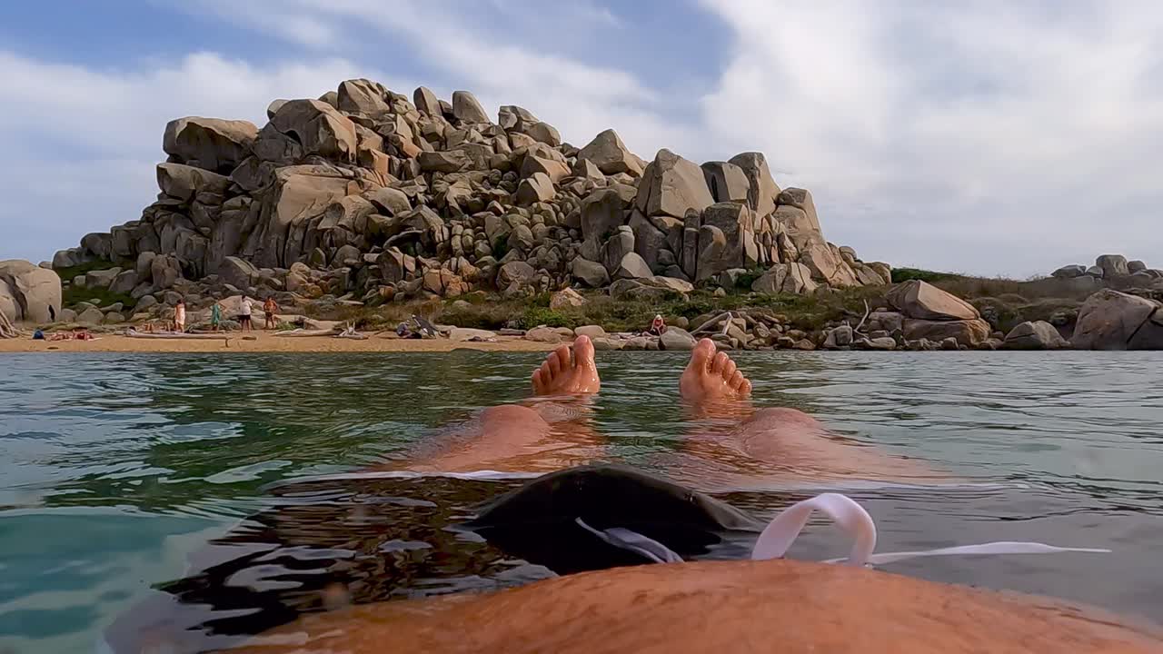 Subjective point of view of man legs and feet relaxing while floating on calm sea water of Lavezzi lagoon on Corsica island in France
