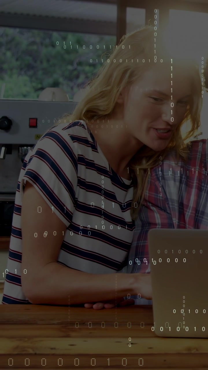 Woman typing on laptop at counter animating binary overlay, partner watching, working for tech